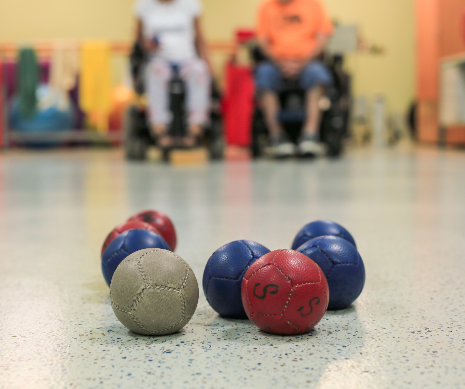 White, red and blue boccia balls on the florr with a blurred image of participants in the background