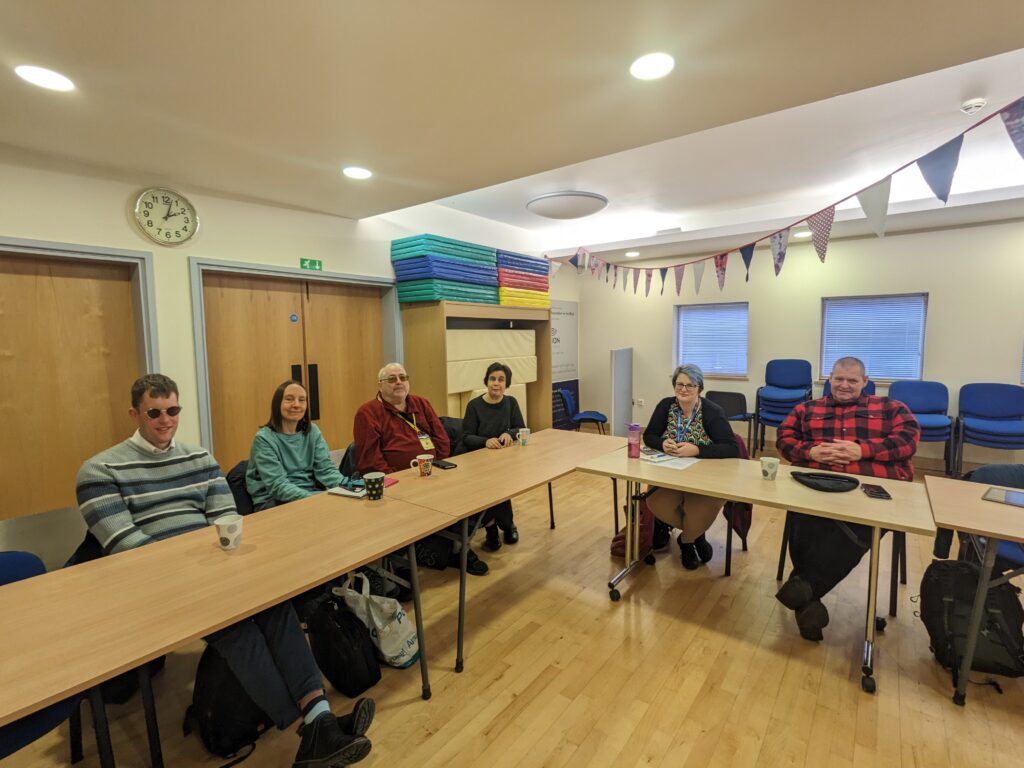 Six of the workshop participants sitting behind desks, smiling at the camera.