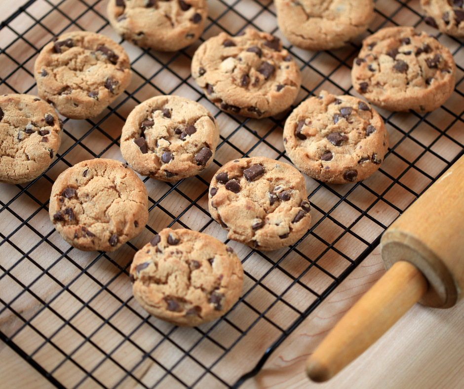 Chocolate chip biscuits lined up on a cooling rack with a rolling pin on the right