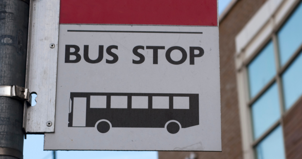Close up of a sign for a bus stop. The sign has the words "bus stop", a graphic of a bus and a red pannel at the top.