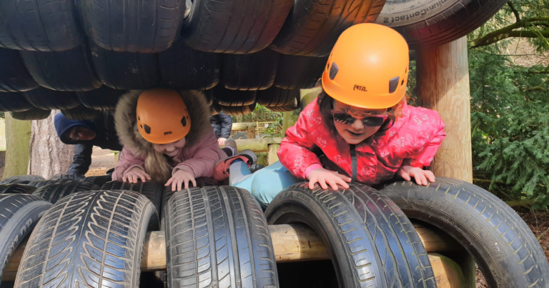 Two girls wearing helmets crawl through a tunnel of tires as part of an obstacle course