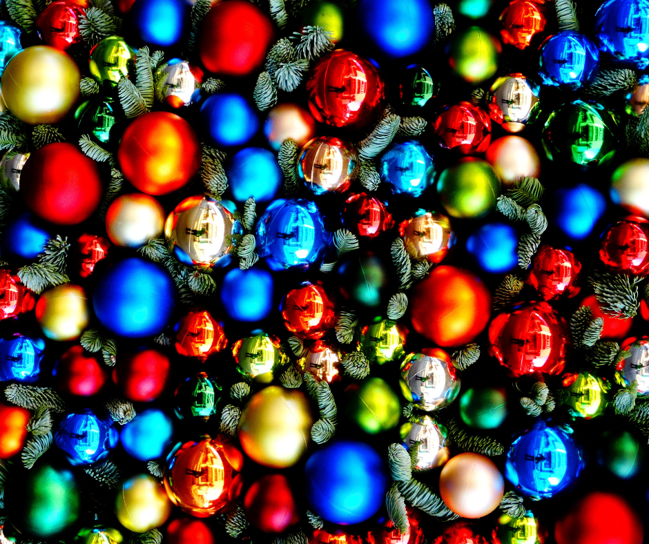 Close up of many multi coloured Christmas baubles between evergreen branches.