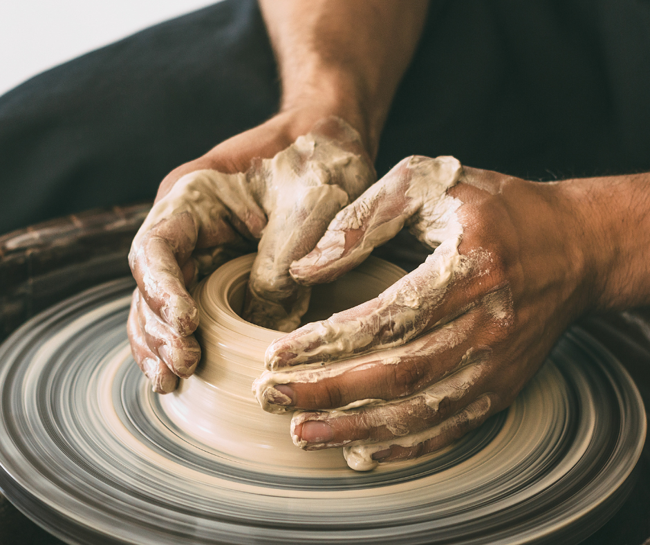 Two hands forming a bowl out of wet clay on a potter's wheel.