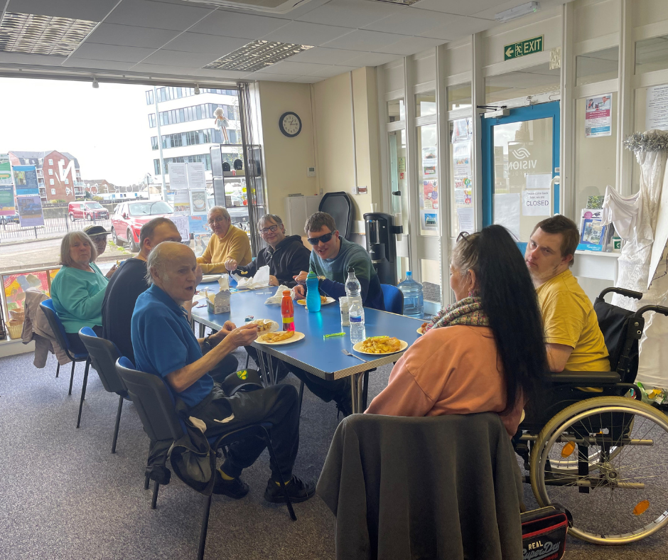 Nine people sitting around a table in the Great Yarmouth Hub enjoying fish and chips as part of Fishy Friday.