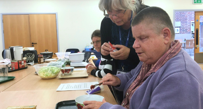 A Community Outreach Worker helps two visually impaired ladies in a cookery class.