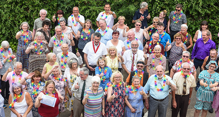 A group of about 40 adults outdoors who are smiling and giving the thumbs up to the camera. The photograph has been taken from above.