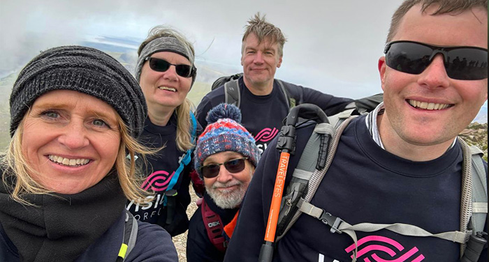A selfie of a group of five people at high altitude wearing hiking gear, backpacks and Vision Norfolk sweatshirts.