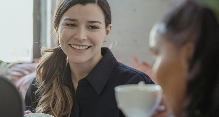 Two ladies drinking from teacups and smiling.