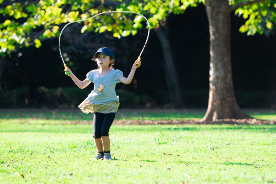 A young girl skipping outdoors in a park.