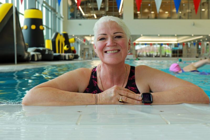 A lady in a swimming pool, leaning on the edge and smiling towards the camera.