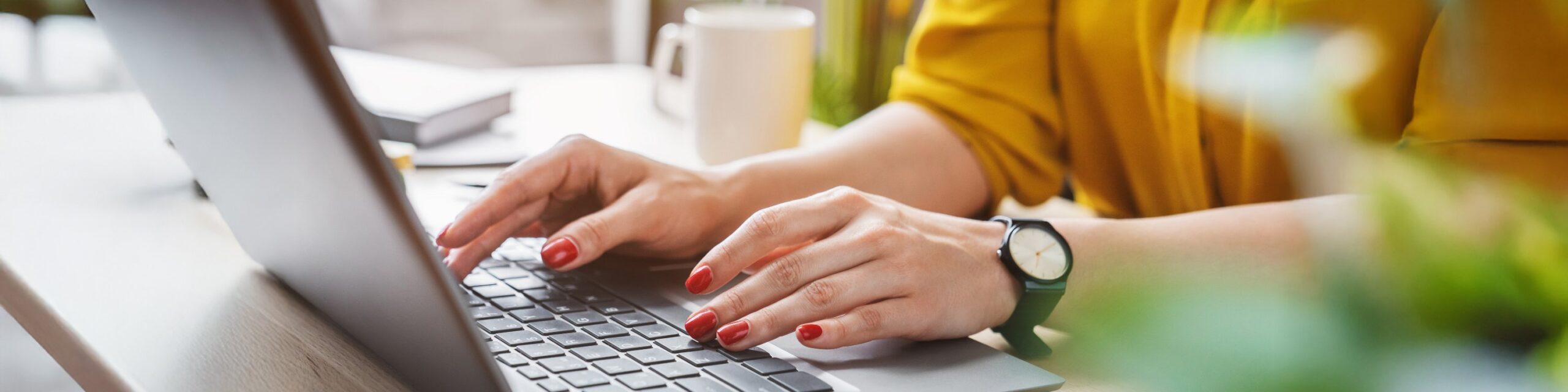 Hands with well-manicured, re-varnished nails, typing on a laptop keyboard on a desk.
