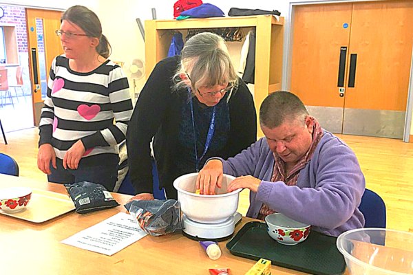 A Community Outreach Worker helps two visually impaired ladies in a cookery class.