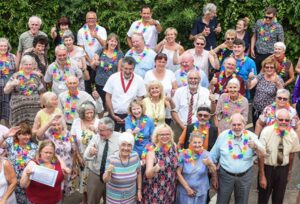 A group of about 40 adults outdoors who are smiling and giving the thumbs up to the camera. The photograph has been taken from above.