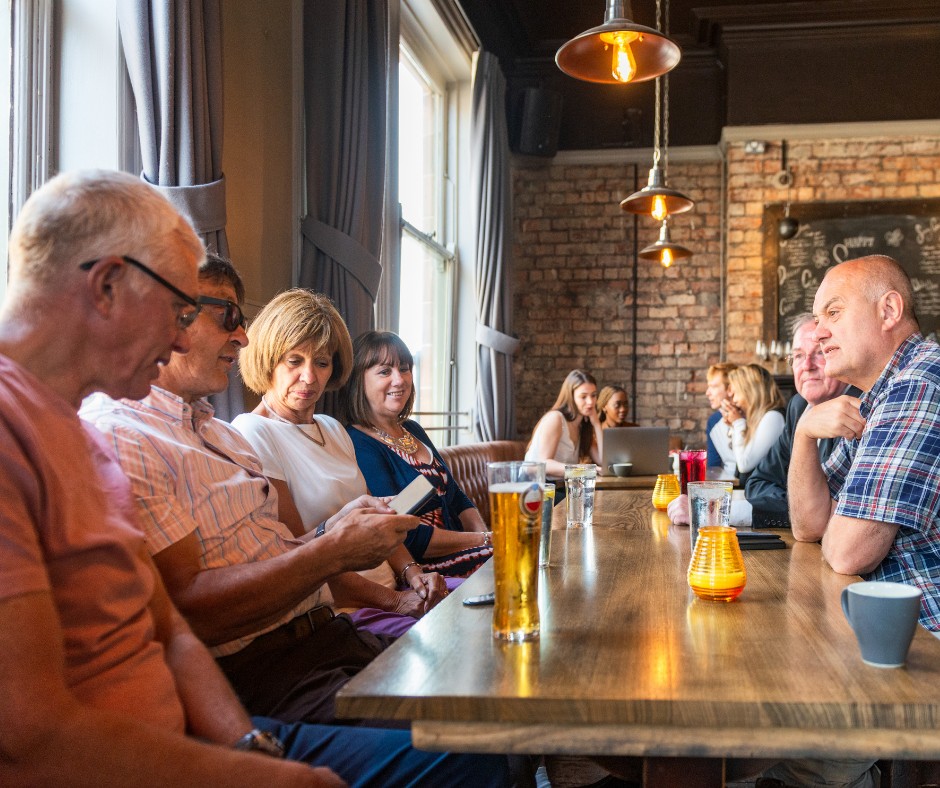 A group of six people sat around a table and chatting in a busy pub.