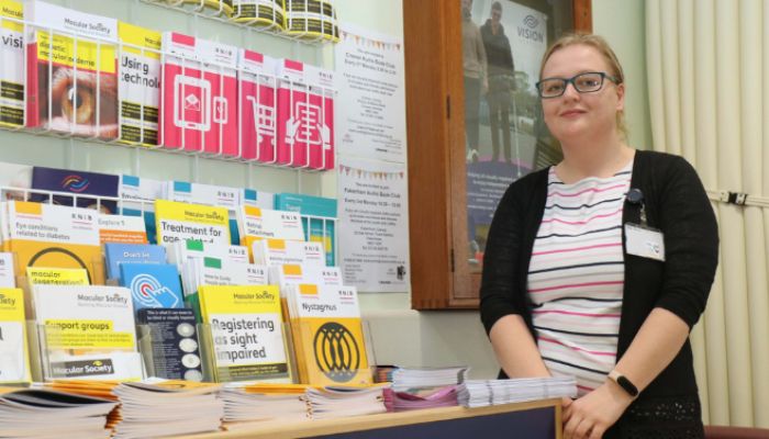 One of our Eye Clinic Liaison Officers stands by a rack containing various information leaflets.