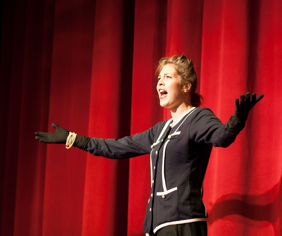 A lady wearing black is singing in front of red stage curtains.