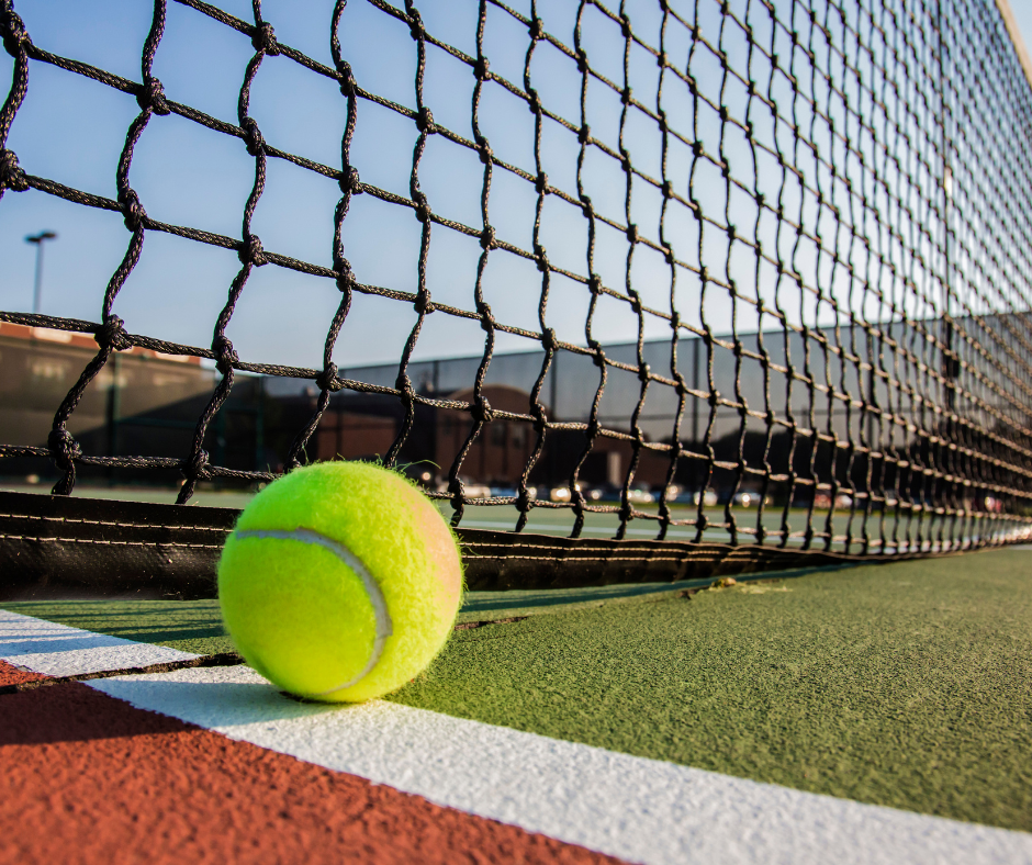 Close up of a green tennis ball at the bottom of the net on a tennis court.