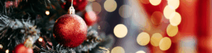 Close up of a red bauble on a decorated Christmas tree. On the right the background is blurred of lights.