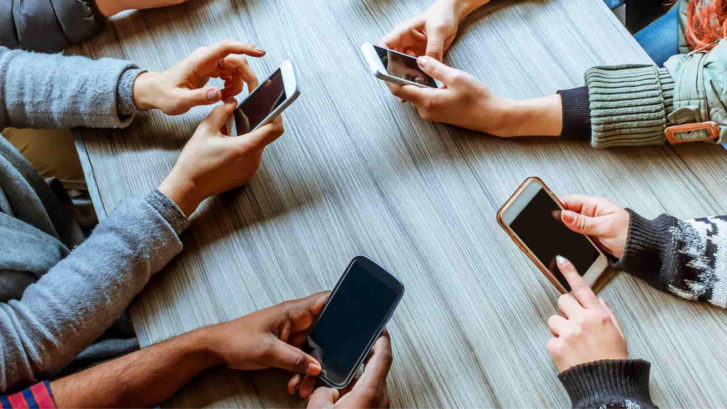 Four people sitting around a table holding smartphones.