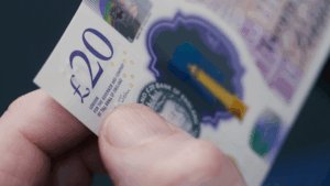 A hand feeling the tactile dots on the upper left corner corner of a £20 note.