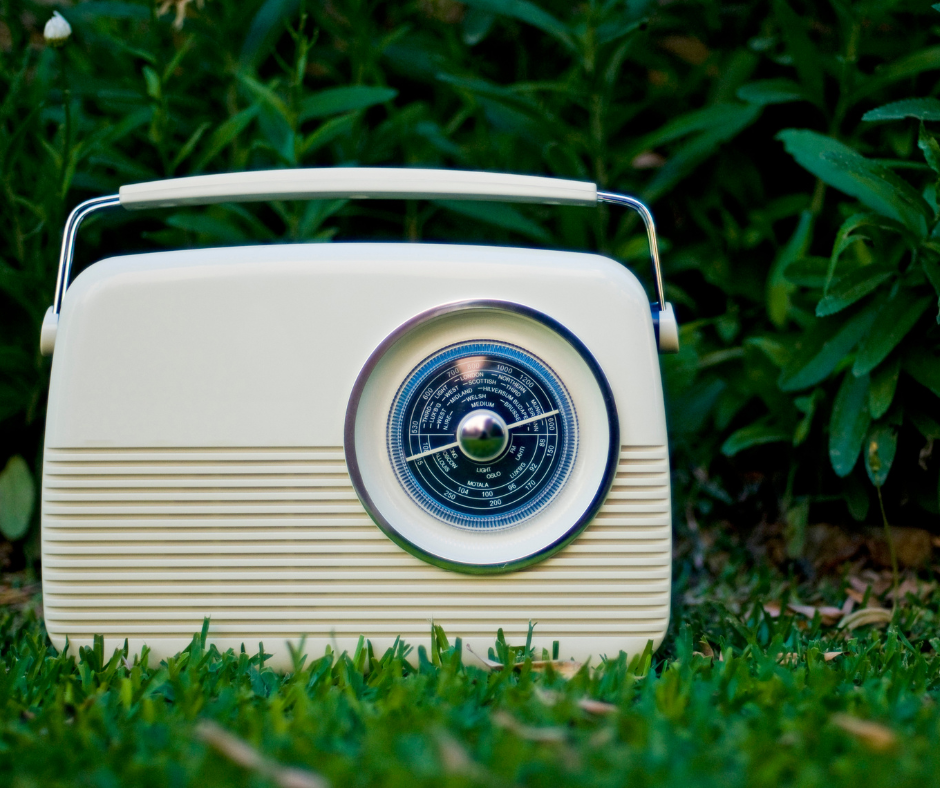 A white radio sitting on grass by some bushes.