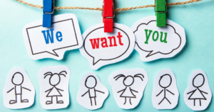Cut out stick figures on a blue background. Above them are the words "We want you" hung up on a wire with clothes pins.